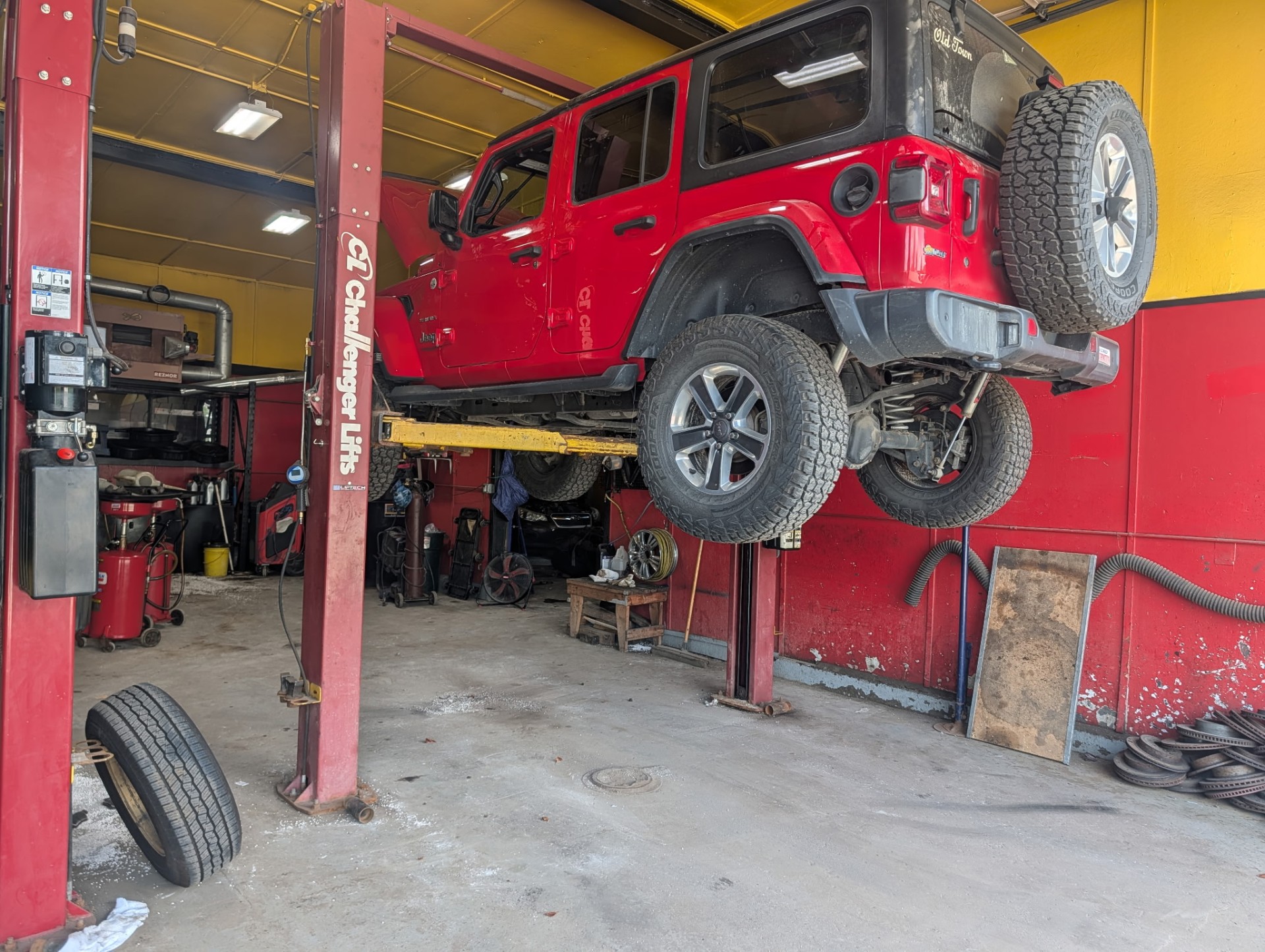 Red Jeep Wrangler up on a Challenger lift inside the R&R Auto Repair bay